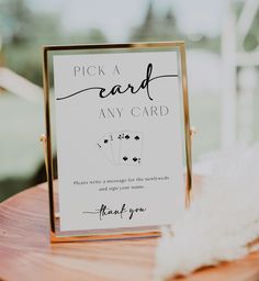 a card that says pick a card any card on top of a wooden table next to a white feather