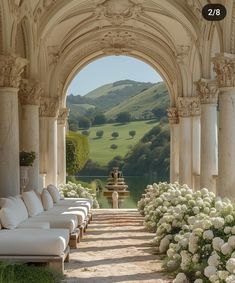 an archway leading to a garden with white flowers and benches in the foreground, surrounded by lush green hills