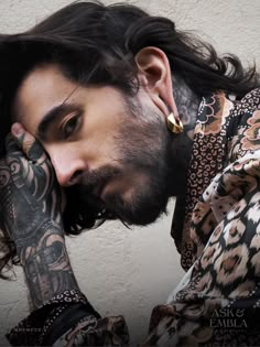 a man with long hair and tattoos on his arm holding his hand to his face