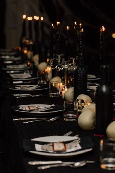 a long table is set with black and white plates, silverware, candles and wine bottles