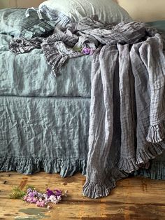 an unmade bed with blue linens and purple flowers