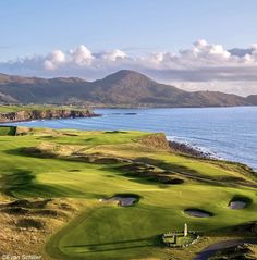 an aerial view of a golf course with the ocean and mountains in the back ground