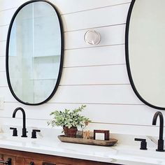 two oval mirrors on the wall above double sinks in a bathroom with wood cabinets and white walls