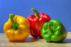 three different colored peppers sitting on top of a wooden table