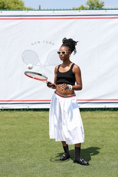 a woman holding a tennis racquet on top of a grass covered field in front of a banner