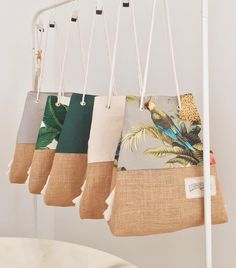 several bags hanging from a white rack in front of a table with a plant on it