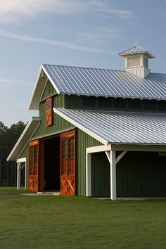 a green and white barn with red doors