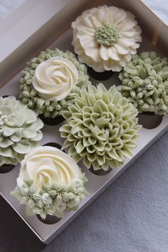 cupcakes with white frosting and green flowers in a box