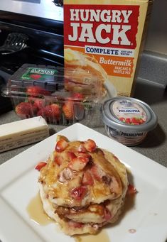 a stack of pancakes sitting on top of a white plate next to a box of fruit