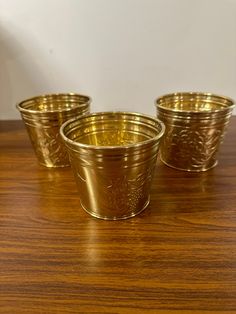 three brass cups sitting on top of a wooden table