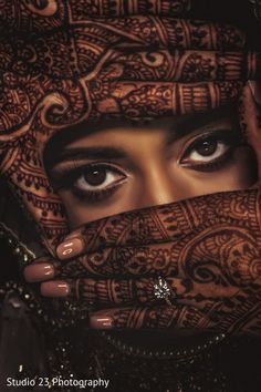 a close up of a woman with henna on her face and hands covering her eyes