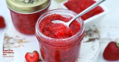 strawberry jam in a glass jar with a spoon next to it and two small white bowls full of strawberries