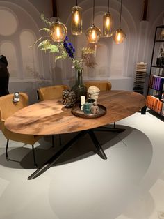 a round wooden table with chairs around it in a room filled with books and vases