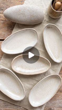 a table topped with lots of white plates next to a cup and wooden spoons