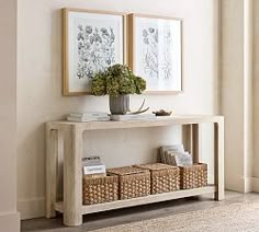 two framed pictures on the wall above a console table with baskets and flowers in it