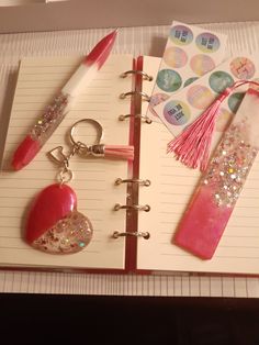 an open notebook with pink and silver items on it, including a keychain