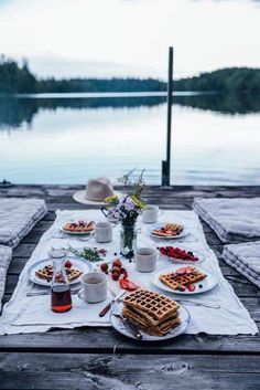 a table topped with waffles and fruit on top of a wooden table next to water