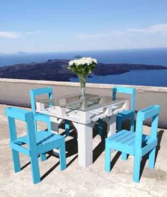 there is a table and four chairs on the balcony overlooking the ocean with flowers in vase