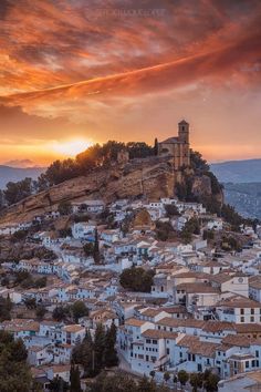 the sun is setting over an old town on top of a hill with white buildings