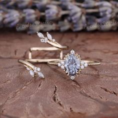 two gold rings with an oval cut diamond surrounded by smaller round diamonds on a piece of wood