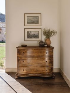 a wooden dresser sitting in the corner of a room with pictures on the wall above it