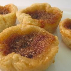 four small pastries on a white plate with some brown stuff in the middle,