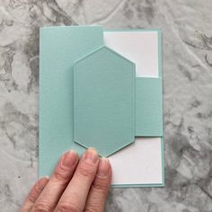 a hand is holding the corner of a folded card on top of a marble surface