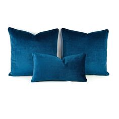 two blue velvet pillows with white piping on the back and one in dark blue