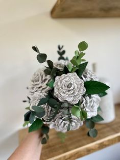 a bridal bouquet is being held by someone's hand on a wooden table