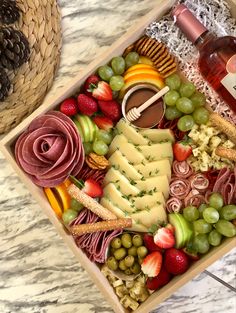 a wooden box filled with different types of cheese and fruit next to a bottle of wine