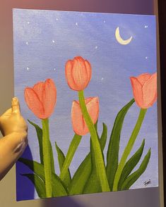 a person holding up a painting with pink flowers on it and the moon in the sky