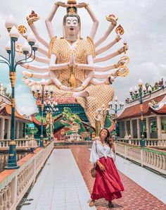 a woman standing in front of a large buddha statue at the entrance to a temple