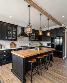 a large kitchen with black cabinets and wooden counter tops, along with stools that match the hardwood flooring