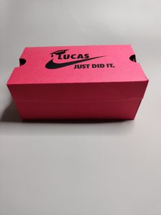 a pink nike box with the words tucas just did it printed on it, sitting on a gray surface