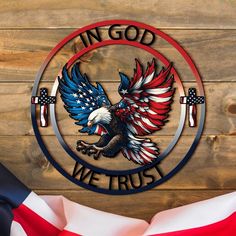 an american flag and the words in god we trust on a wooden background with a metal eagle emblem