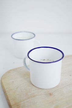 two white cups with blue rims sitting on a cutting board next to each other