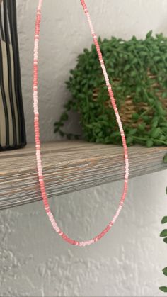 a pink beaded necklace sitting on top of a shelf next to a potted plant