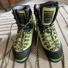 a pair of hiking boots with yellow and black laces sitting on a carpeted floor