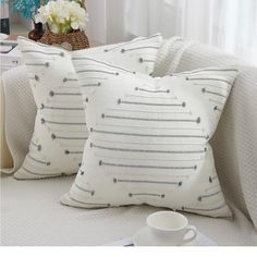 two white pillows sitting on top of a bed next to a cup and saucer