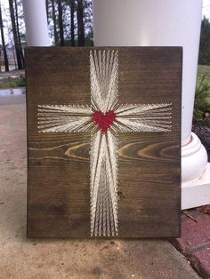 a wooden cross with a red heart on it sitting next to a white pillar and trees