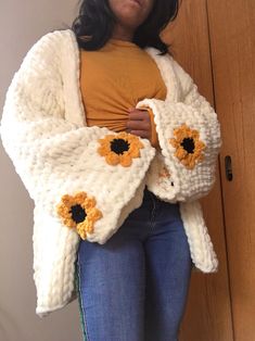 a woman standing in front of a door wearing a crocheted jacket with sunflowers on it