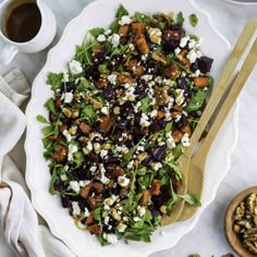 a white plate topped with a salad next to a wooden spoon and cup of coffee