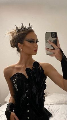 a woman taking a selfie with her cell phone wearing a black dress and tiara