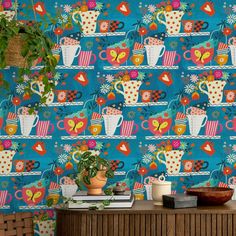 a blue wallpaper with colorful cups and flowers on it, next to a potted plant