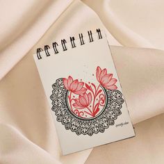 a spiral notebook with red flowers on it sitting on top of a white cloth covered surface