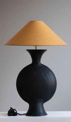 a black table lamp with a beige shade on the base and a cord plugged into it