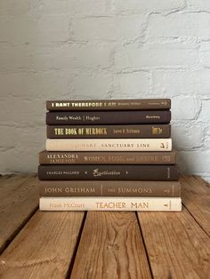 five books stacked on top of each other in front of a white brick wall and wooden table