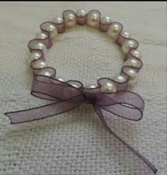 a close up of a bracelet with pearls and ribbon on a white tablecloth background