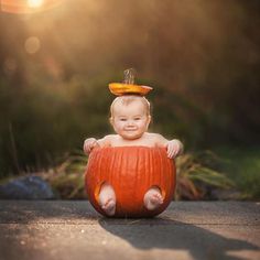 a baby sitting on top of a pumpkin in the middle of an open area with sun shining