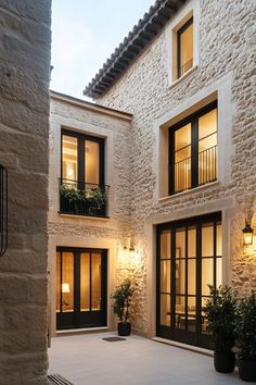 an outdoor courtyard with potted plants and lights on the side of it, surrounded by stone buildings